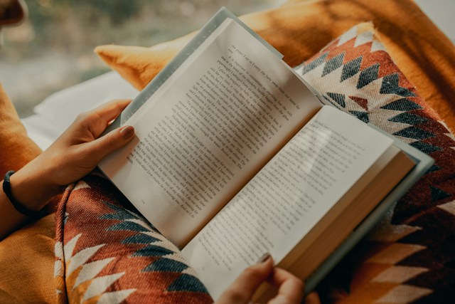 Reader holding an open book on a patterned cushion