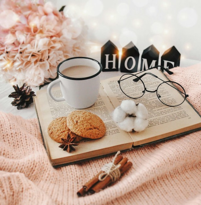 Open book with a mug, cookies and reading glasses on a knit blanket
